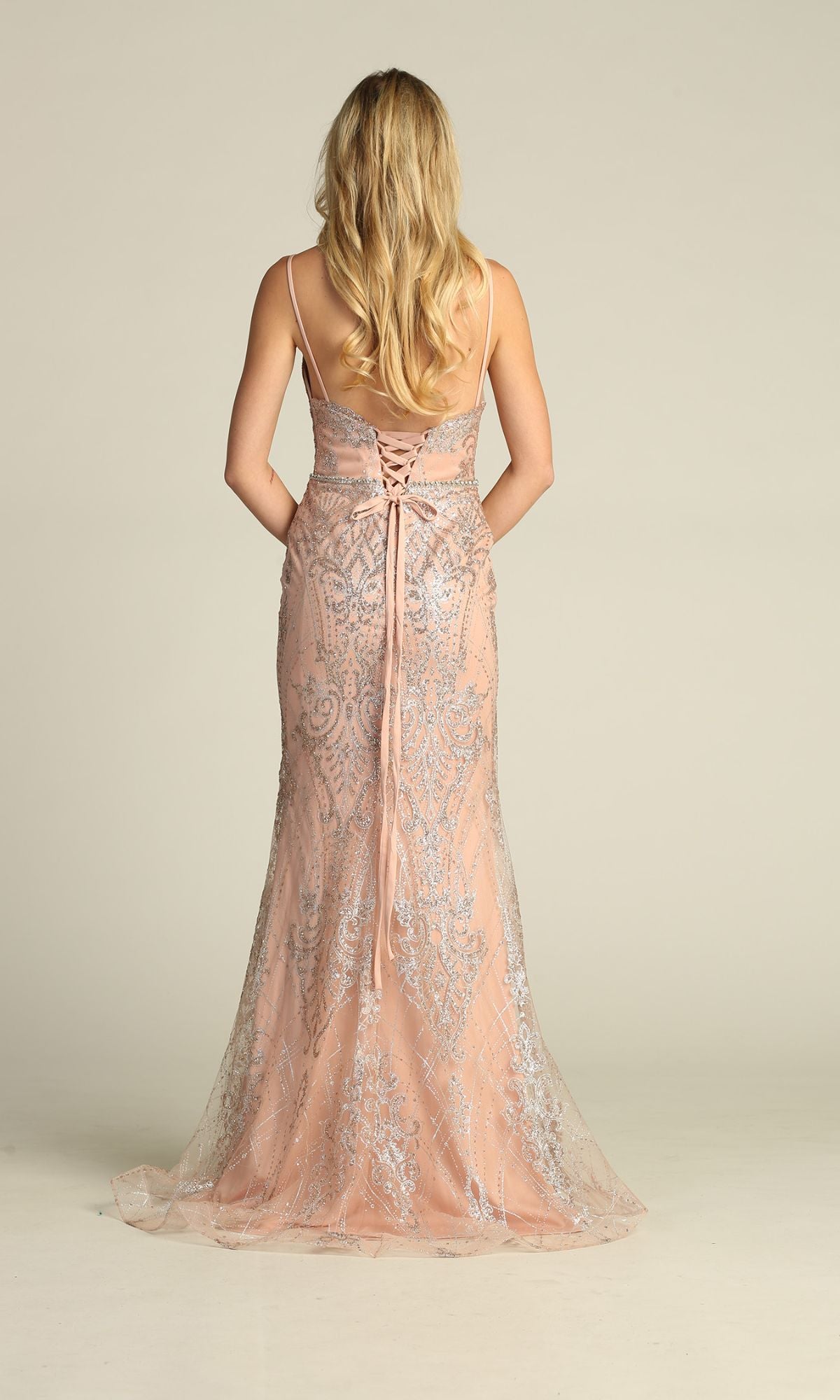 A woman with long blonde hair wears the Chicas CHF3053 Lace-Up Long Glitter Prom Dress in blush pink, featuring silver embellishments and a floor-length design, while standing against a plain background.